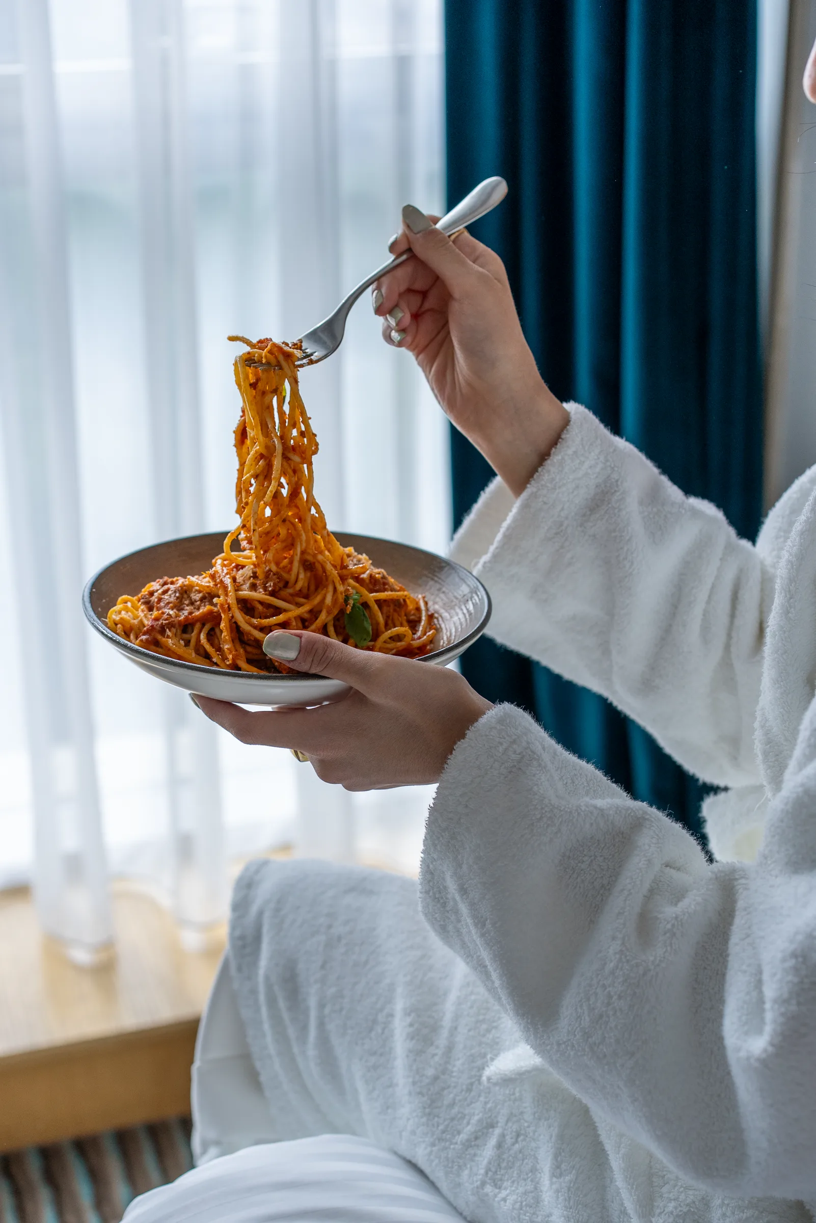 Pencere kenarında bornozlu konuk, elinde bolonez spagetti — oda servisi