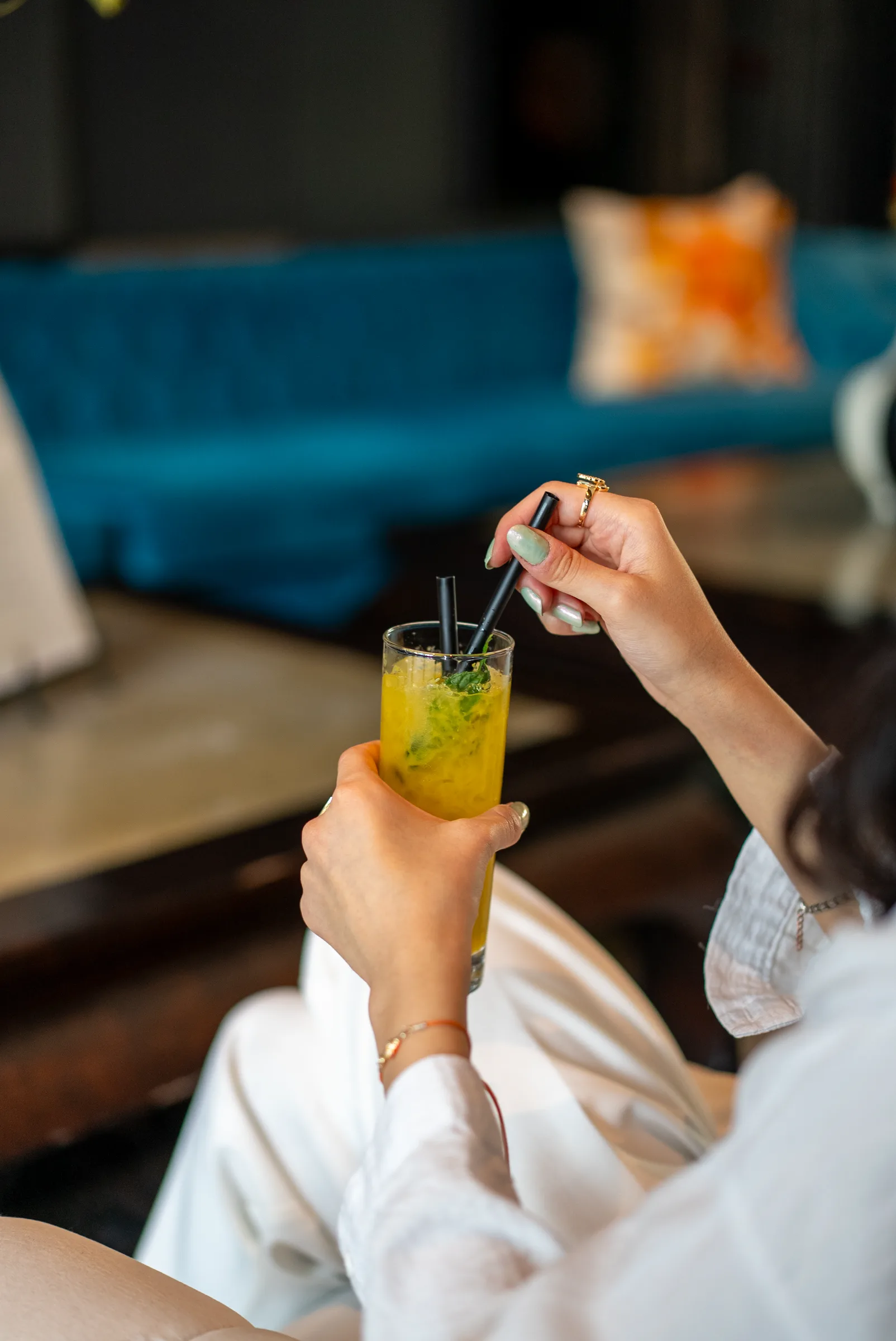 Lounge'da mavi kadife koltuklar önünde kokteyl karıştıran konuk